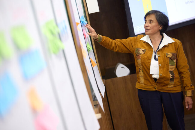 BDC_Cambiar_la_mirada Mujer participando en un taller de BeDoCare, señalando notas adhesivas de colores en un panel durante una dinámica de trabajo colaborativo.