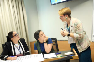 Tres mujeres participan en un taller de BeDoCare, dialogando y compartiendo ideas alrededor de una mesa con materiales de trabajo.