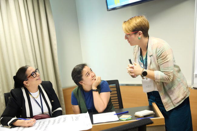 BDC_Deja de mirar. Empieza a cuidar Tres mujeres participan en un taller de BeDoCare, dialogando y compartiendo ideas alrededor de una mesa con materiales de trabajo.