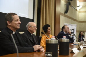 Mesa redonda sobre el origen de BeDoCare, con dos sacerdotes y otros dos participantes durante una conferencia.